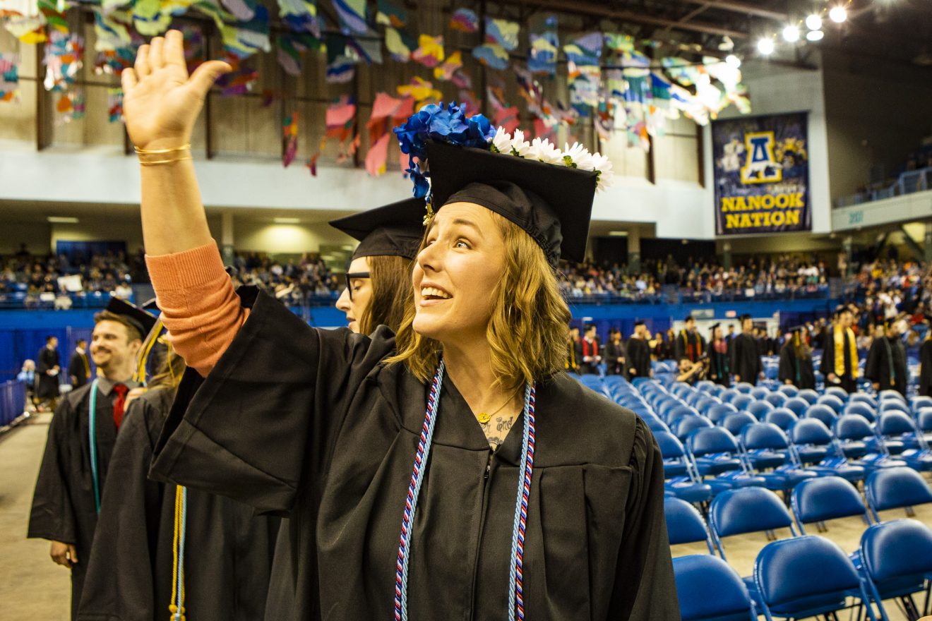 Woman in cap and gown waving during the commencement ceremony.