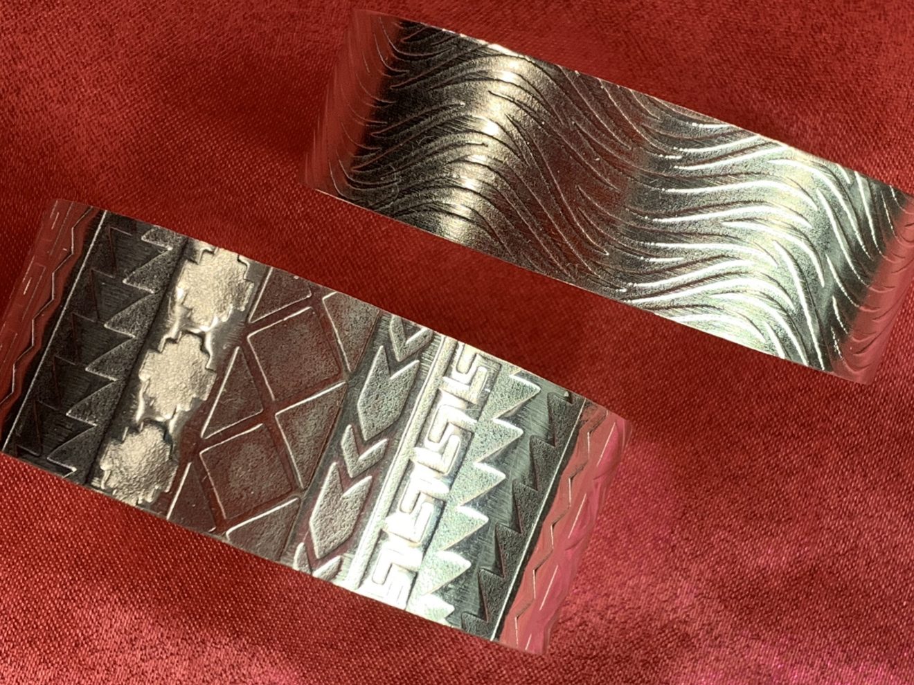 Closeup of two silver cuffs on a red background.