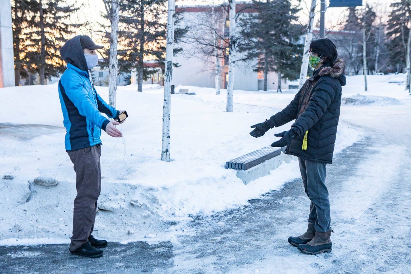 Two students wearing masks greet each other from a distance. It is winter.