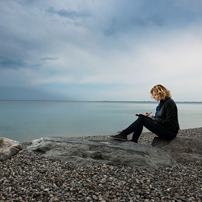 Woman writing while sitting on the beach with the ocean in the background