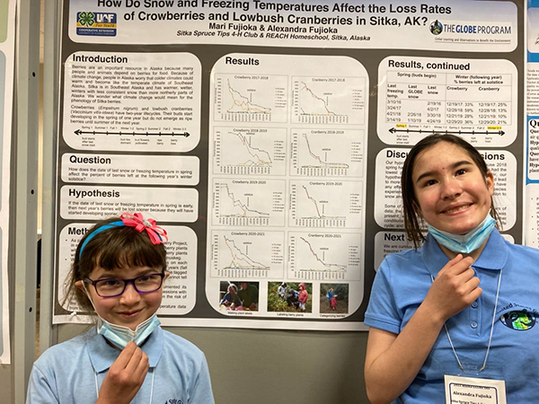 Two young girls stand in front of their research poster
