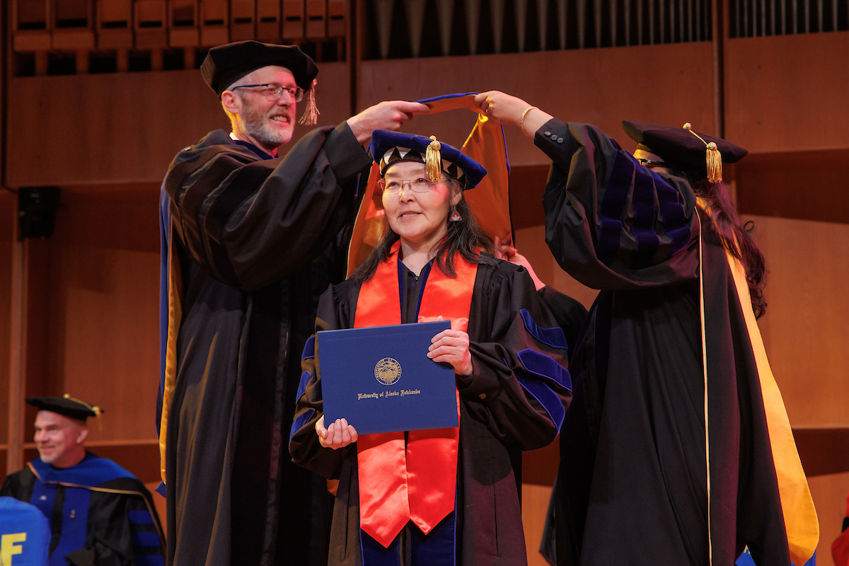 Angass'aq Sally Samson stands while UAF Chancellor Dan White, left, and Provost Anupma Prakash perform the formal Ph.D.  hooding during ceremonies in the Davis Concert Hall on May 5. Samson earned her Ph.D. in Linguistics: Interdisciplinary Studies. UAF Photo by Todd Paris