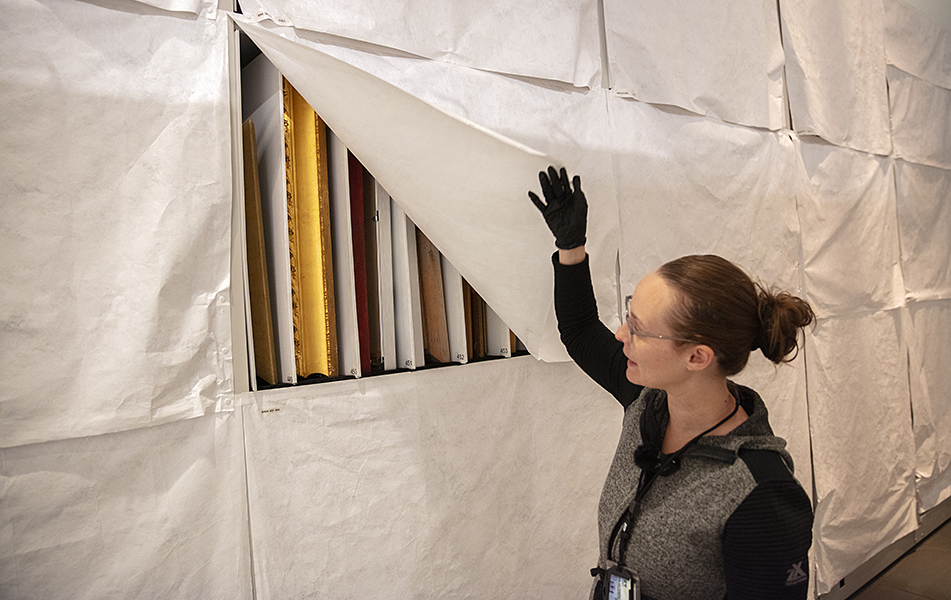 woman holds back curtain revealing artwork in storage