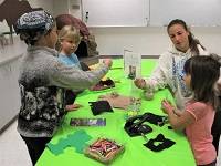 Group of three children and one adult gathered around a table working on craft projects.