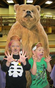 Two children stand in front of a cardboard cutout of a grizzly bear.