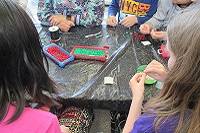 People seen from the back sitting at a table, threading beads to make bracelets.