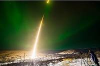 Green aurora lights in the sky, with a bright white light marking the path of a rocket.