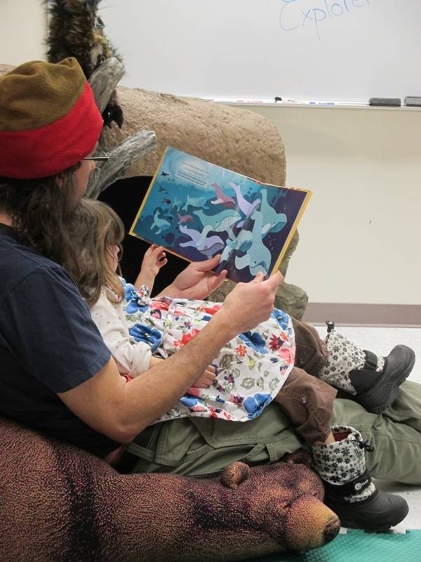 Adult and child sit together in a beanbag chair, reading a picture book.