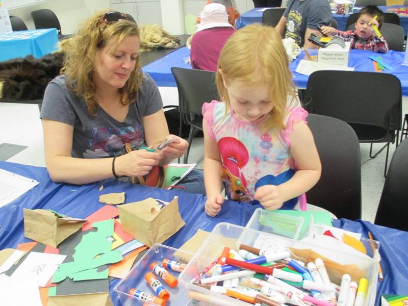 An adult and child sit at a table working on a craft project.