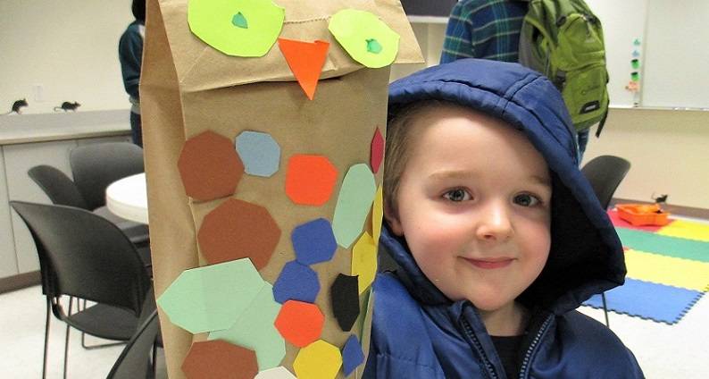 Child holding a owl puppet made from a brown paper bag and construction paper feathers.