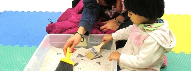 Adult and child uncovering fossils in a box filled with sand.