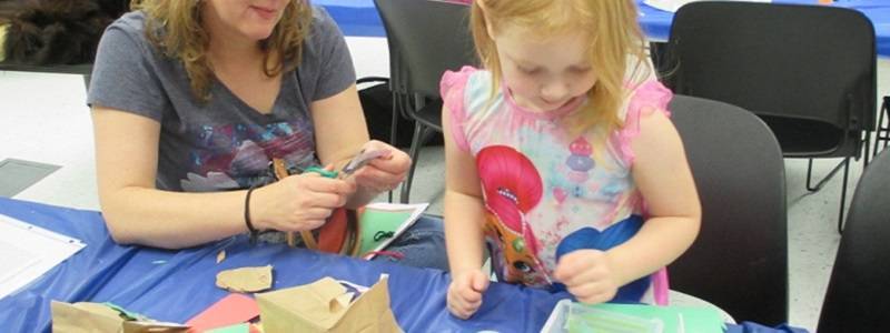 Adult and child sitting at a table with craft supplies in front of them.