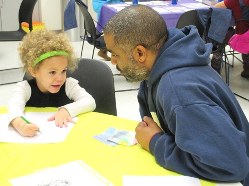 Adult and child sitting at a table, drawing on pieces of paper.