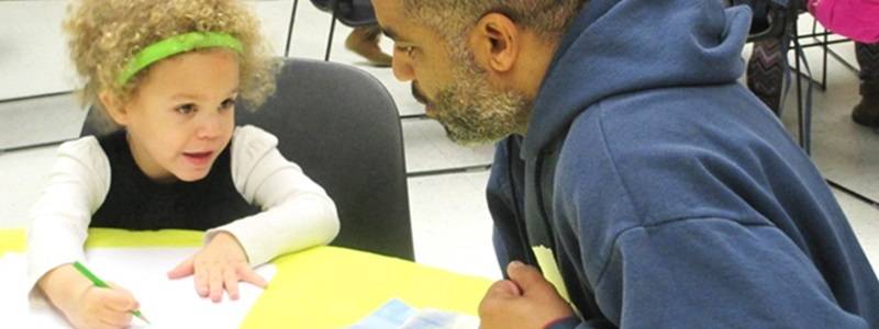 Adult and child sitting at a table, drawing on pieces of paper.