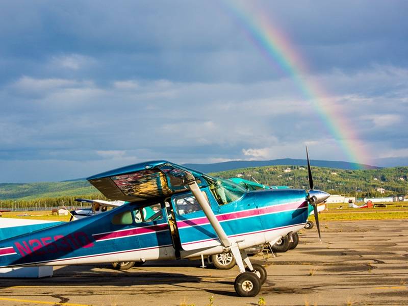 Propeller plane sitting on a runway, with a rainbow in the sky behind it..