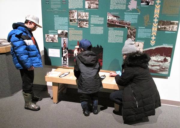 An adult and two children work on a puzzle in a museum gallery.