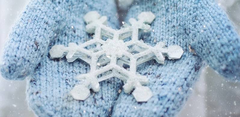 Close up of a snowflake on a pair of blue mittens.