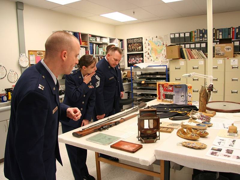 Three people in military uniforms looking at a various of museum objects on a table.