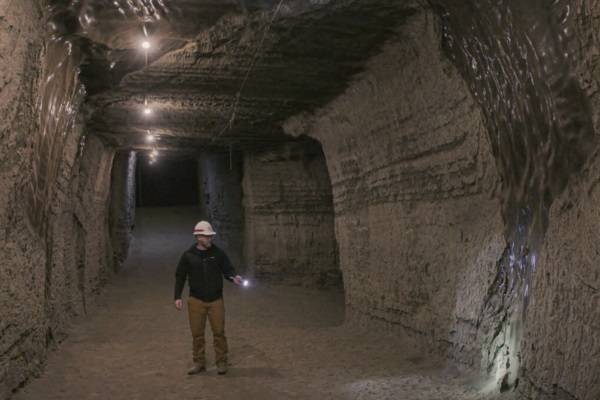 Person standing in a tunnel, wearing a hard hat and holding a flashlight.