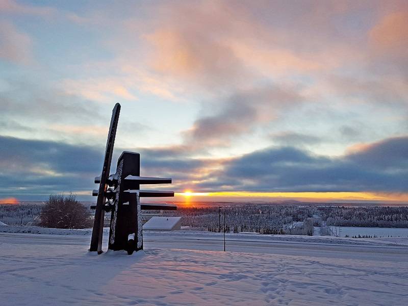 Sun rising  over a snowy landscape, with an abstract black sculpture in the foreground.
