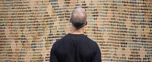 Person wearing a black sweatshirt, seen from the back, looking at a woven artwork.