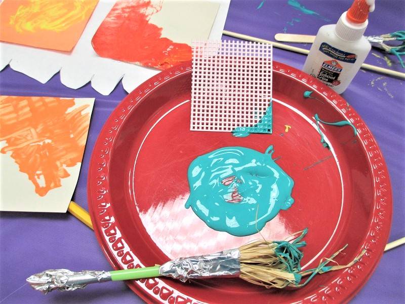 Homemade paintbrush on a red paper plate, next to a circle of light blue paint.
