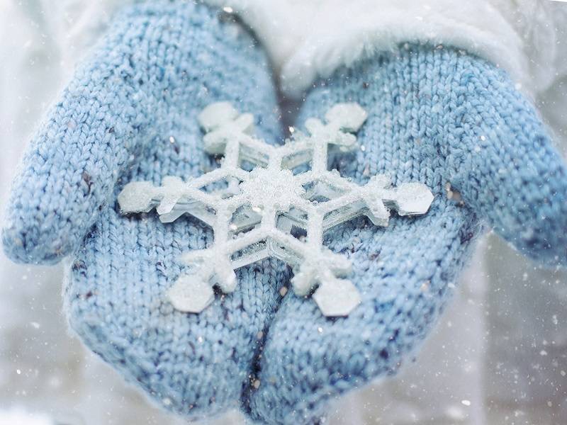 Close up on a pair of blue mittens cradling a snowflake.