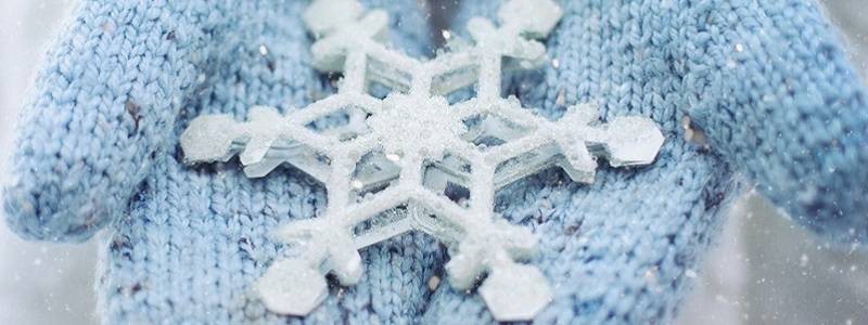 Close up on a pair of blue mittens cradling a snowflake.