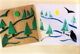 Piece of cardboard with pieces of craft foam in the shape of conifer trees, next to a piece of paper showing a winter scene, created with the tree stamps.