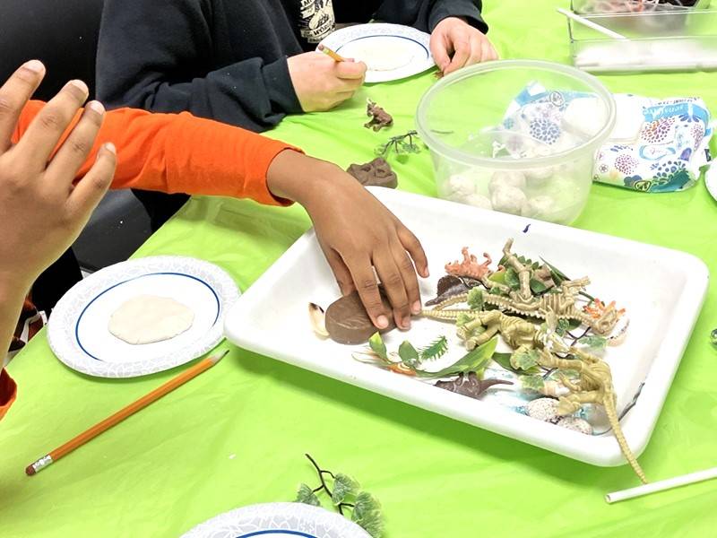 Close up of a hand pressing plastic dino figurines into clay to make model fossils.