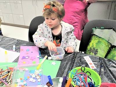 A young child sits at a table, decorating construction paper with star-shaped sequins.