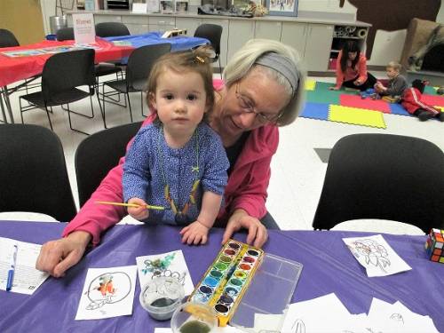 An adult and child sit at a table painting with watercolors.