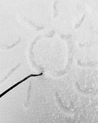 A drawing of the sun carved in snow, with a stick next to it.