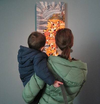 Adult holding a child and looking at a carved artwork by Sara Tabbert.