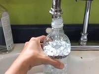 Hand holding a bottle and filling it from a faucet.