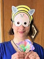 Person wearing a bee mask and holding a colorful paper flower.