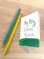 A small booklet with the words "My Big Ideas Book" written on the front. Two colored pencils are next to the booklet.