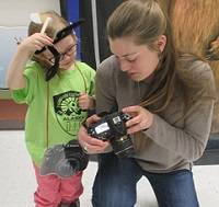 Student kneeling next to a child and showing a camera to the child.