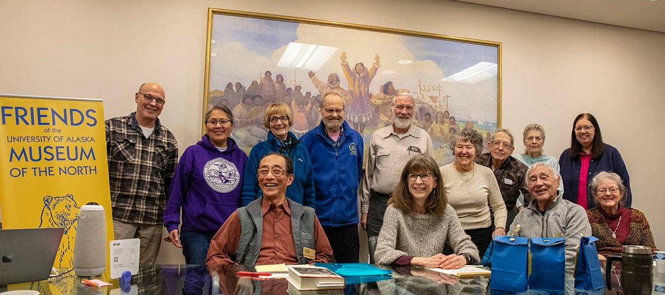 Group of people in a conference room, some standing and some sitting. A banner to the left of the group reads "Friends of the University of Alaska Museum of the North." 