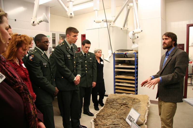 Group of people wearing military uniforms, looking at a large fossil. Curator of Earth Sciences Pat Druckenmiller is talking to the group.