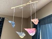 Songbird mobile: four brightly colored paper cutouts of birds tied to two chopsticks and hung from the ceiling.