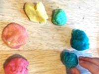 Hand arranging balls of colored play dough in a circle to represent a color wheel.
