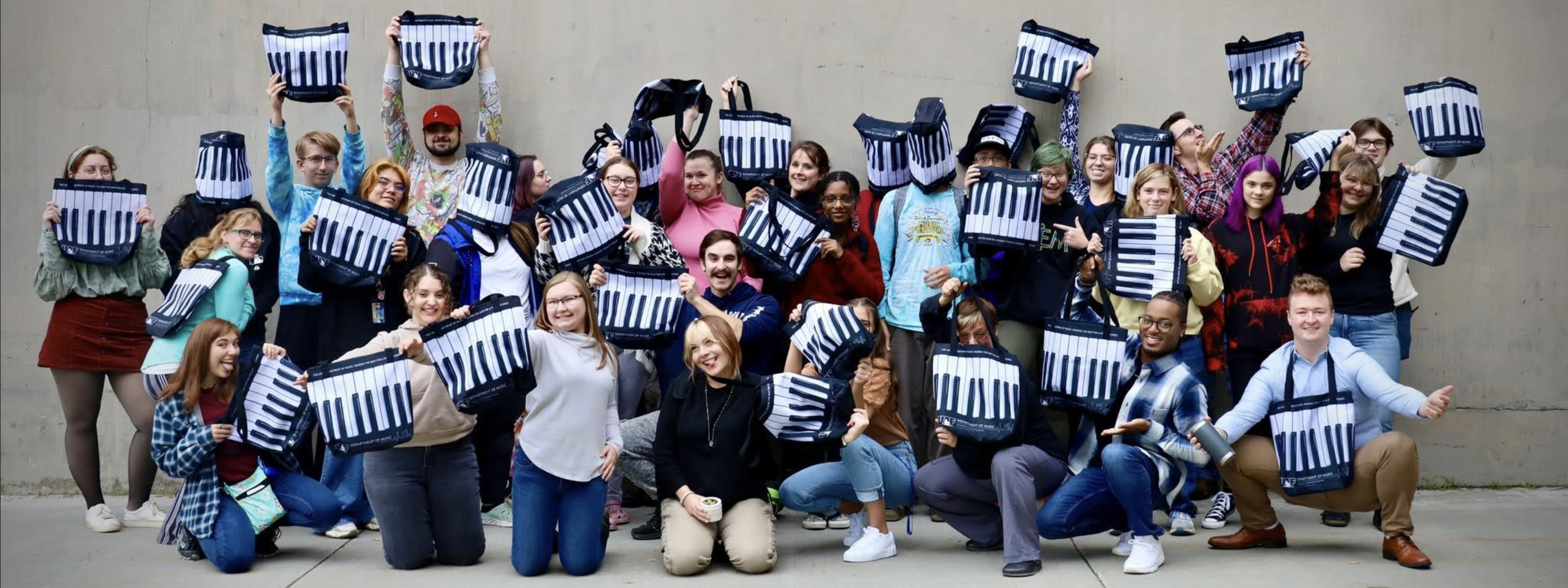 Music students hold up piano-themed tote bags. UAF Photo by Jaunelle Celaire