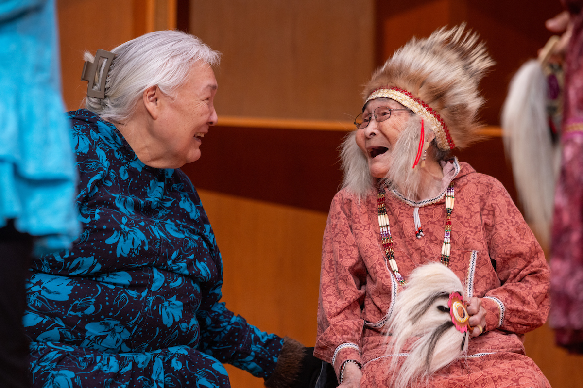 Teresa Pingayak, left, and Cecelia Andrews, right, of Chevak, share a laugh while performing with the Pingayak Dancers and Friends during the 50th annual Festival of Native Arts Friday, February 23, 2024. UAF Photo by Eric Engman