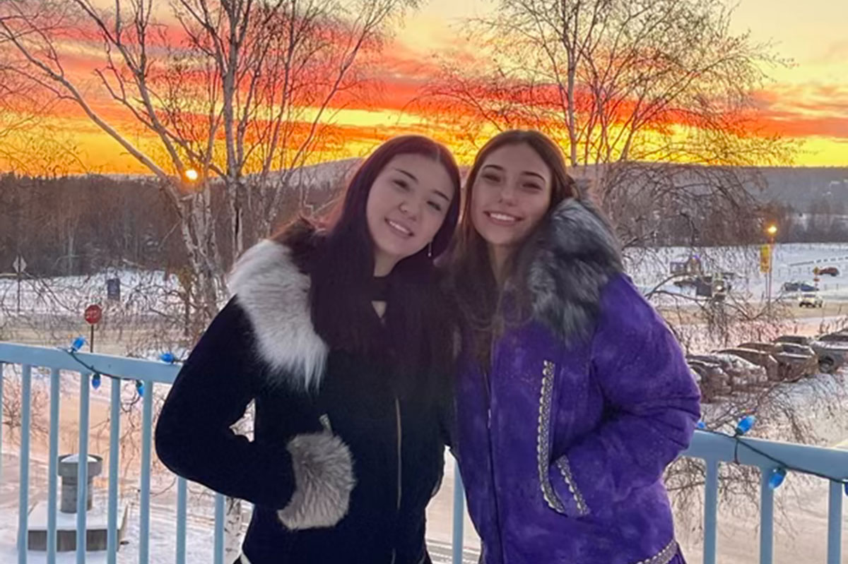 Brenna poses with a friend in front of a sunset on the UAF Troth Yeddha Campus in Fairbanks