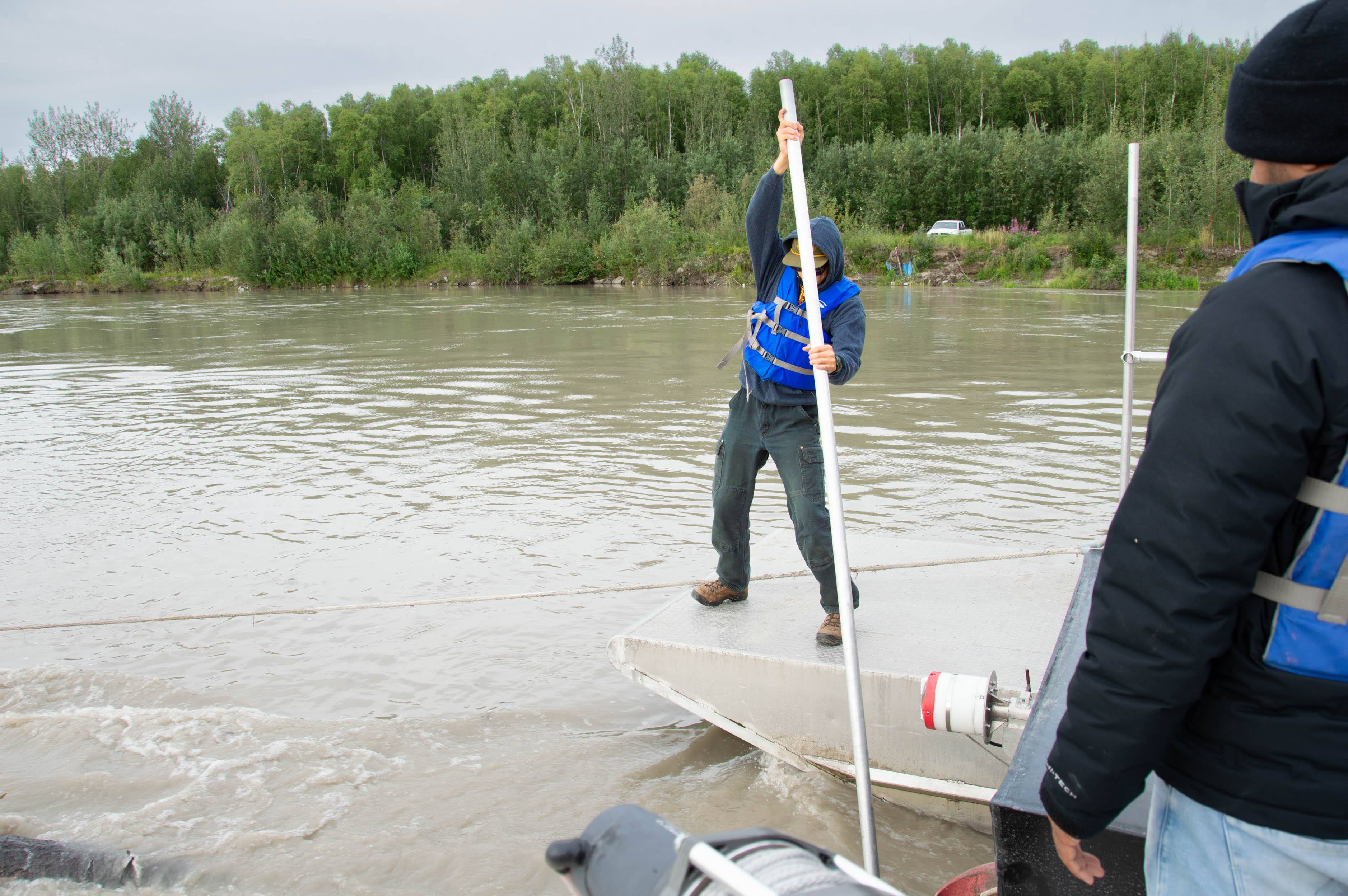 Person stands on a boat with a pole in the river