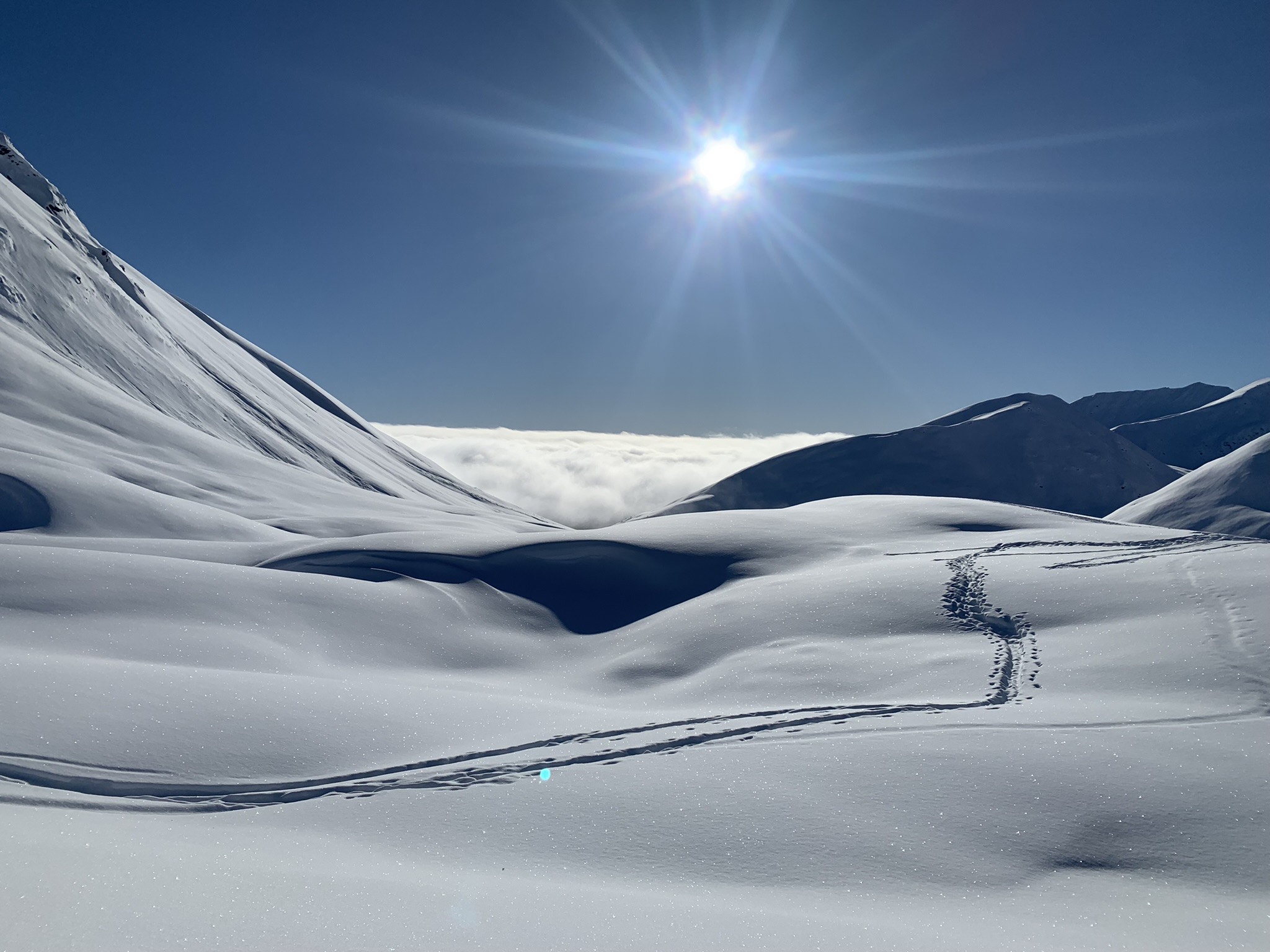 A brilliant sun shines over a hilly and snowy landscape with ski tracks shown across the foreground