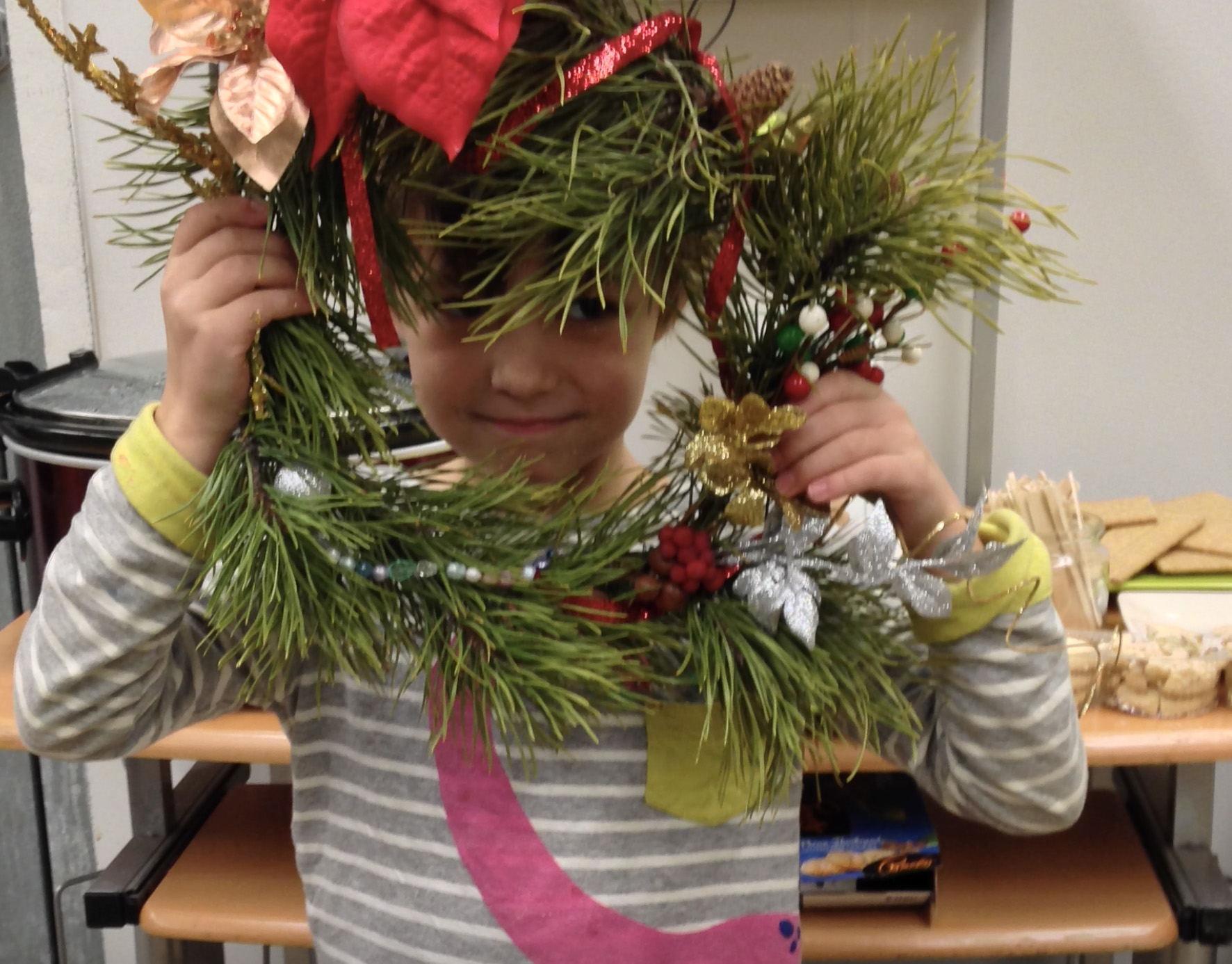 A boy peers through a circular wreath made with shiny bows and tree boughs