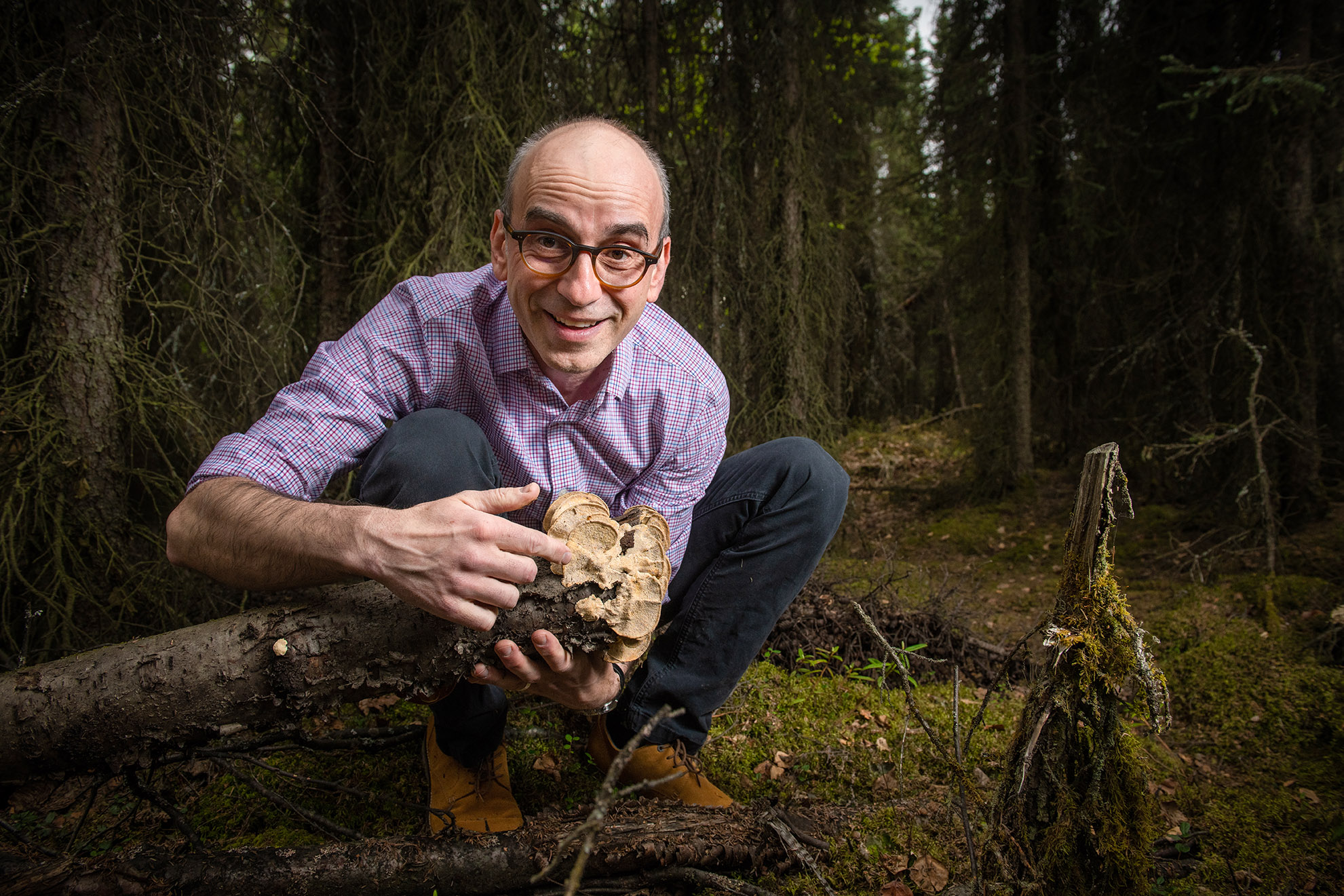 A man holds up a bunch of fungi in a heavily wooded area.