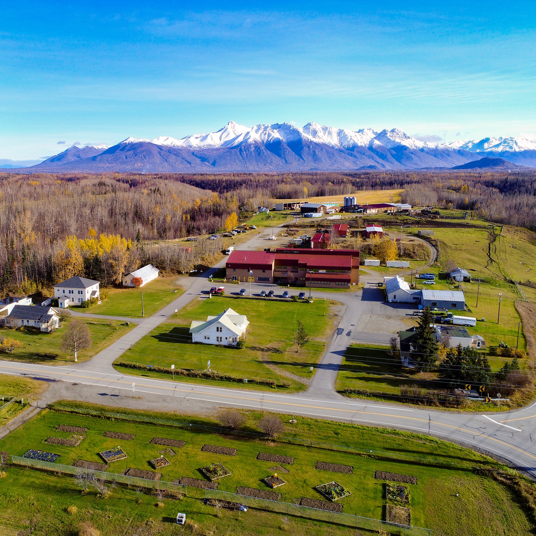 An aerial view of gardens, barns and other farm buildings with snow-capped mountains in the background.